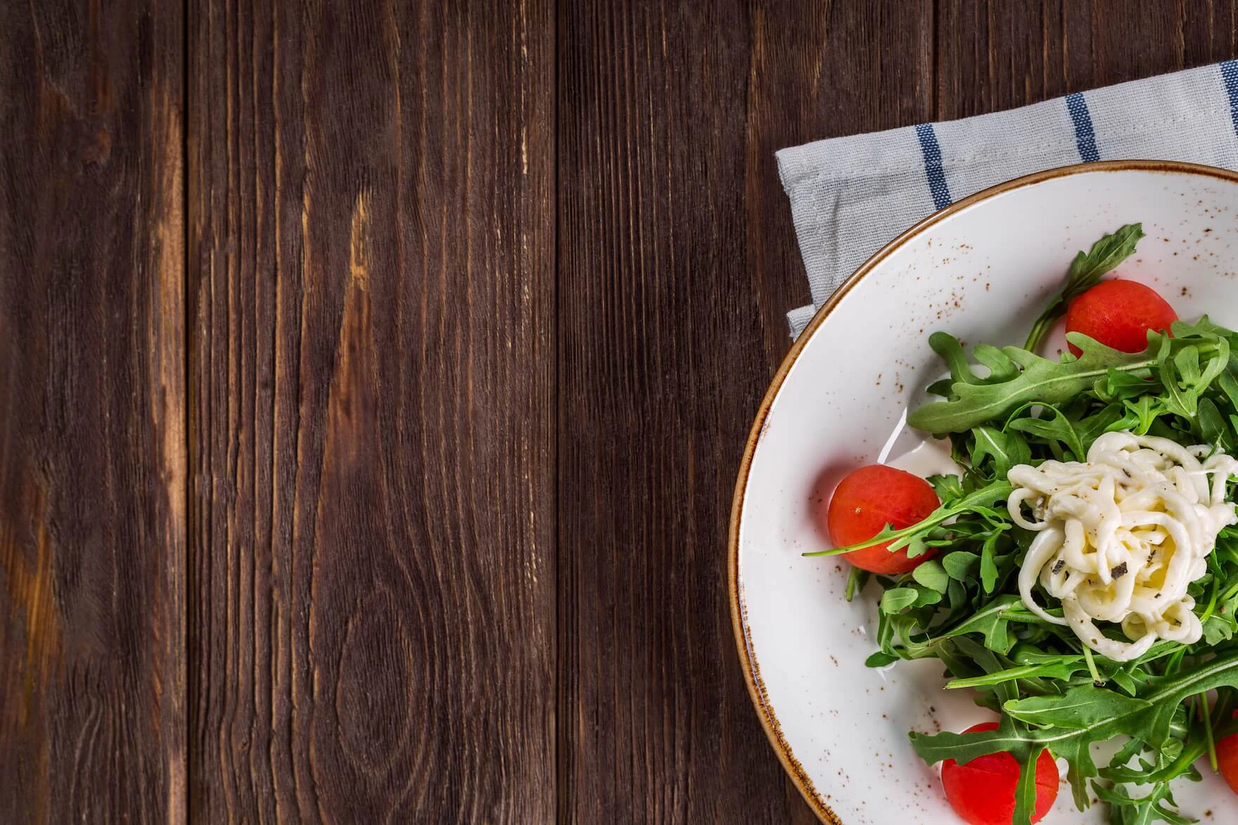 Teller mit Rucola, Tomaten und Nudeln auf Holztisch