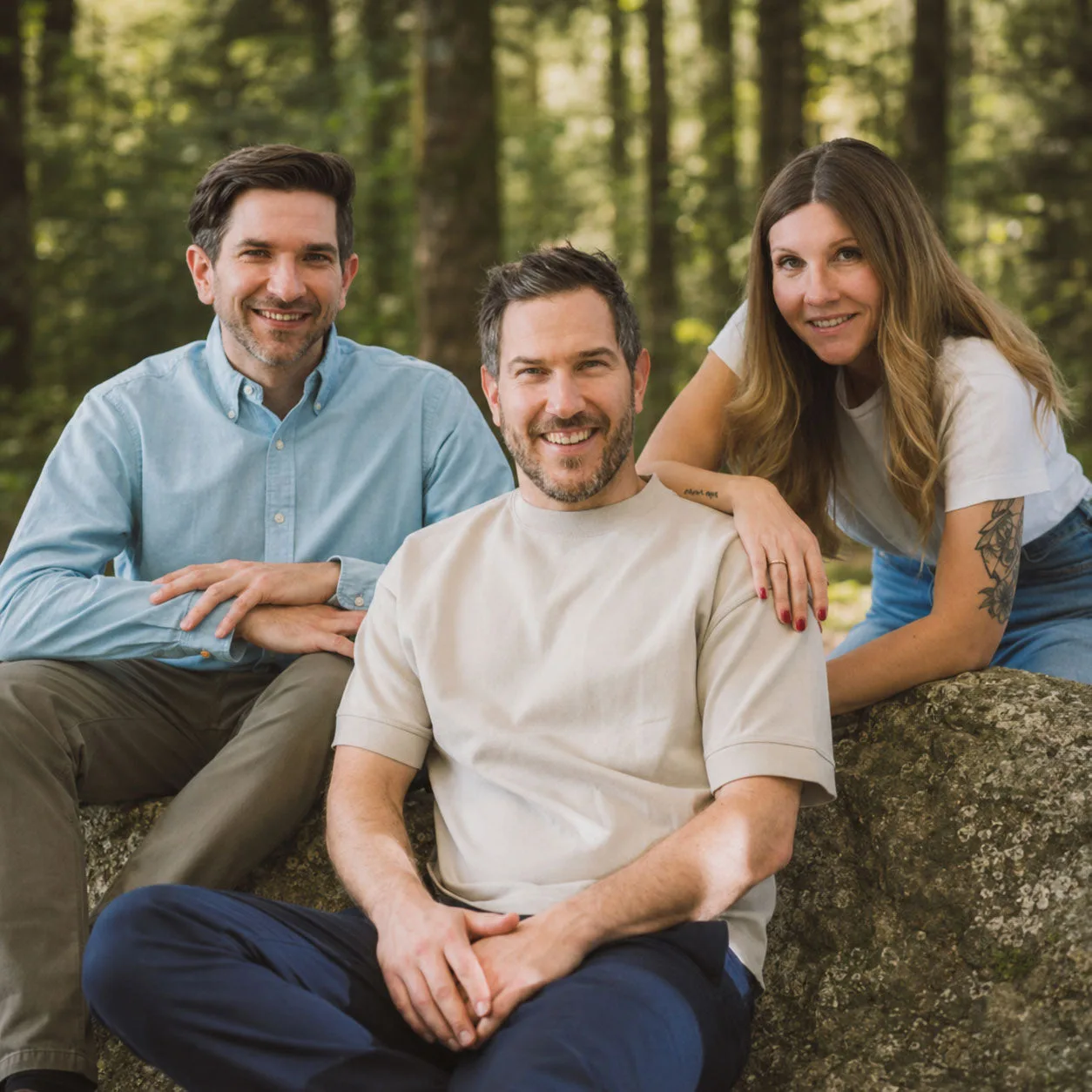 Die drei Goldblatt-Gründer Stephan, Matthias und Mel sitzen lächelnd auf einem Felsen im Wald